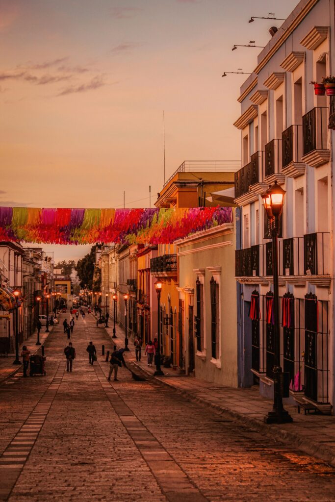 Services Colorful street scene in Oaxaca City featuring colonial buildings and festive decorations during sunset.